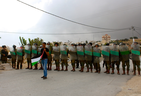 2014-02-25-EstherKilchherr_Bethlehem_2013_ApalestinianinfrontoftheroadblockbyIsraelisoldiersduringAlMasarademonstration.jpg