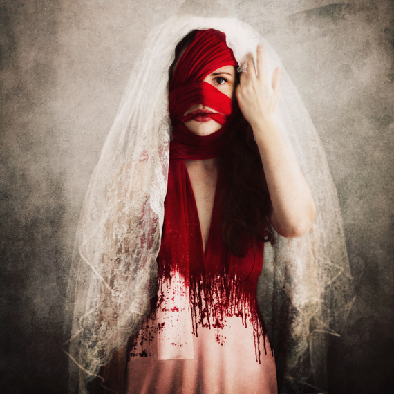 Conceptual Fine Art by Jen Kiaba of a bride wrapped in bloodied bandages, lifting her veil to stare at the viewer