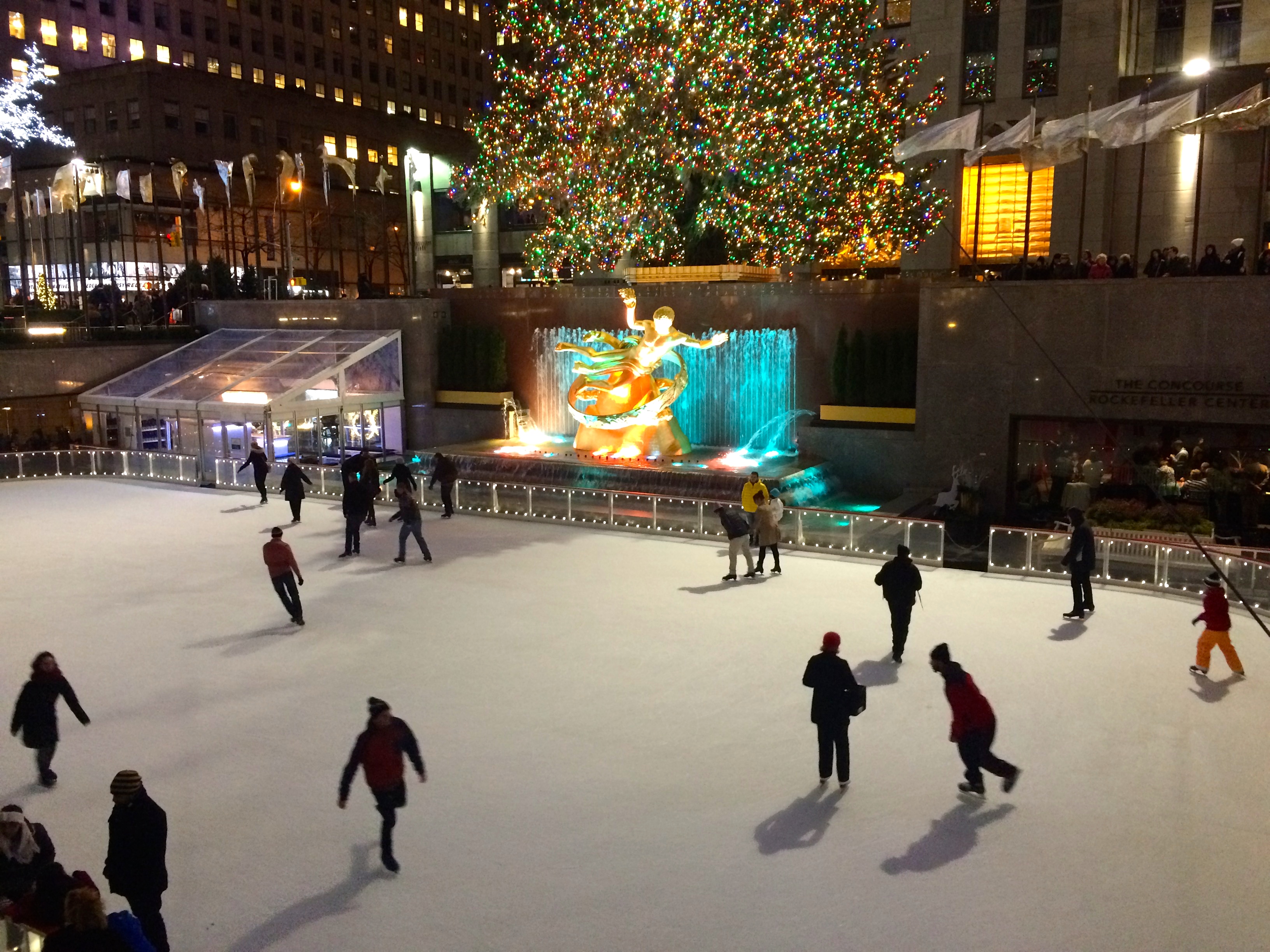 Below the tree, skaters glide around the iconic ice rink; bit players in th...